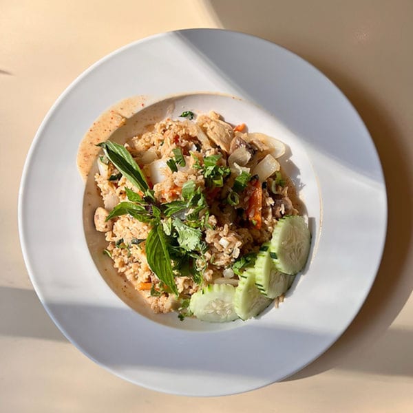 Laos fried rice with chicken, vegetables, and fresh herbs, garnished with cucumber slices.