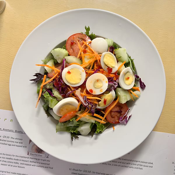 A vibrant Lao salad with lettuce, tomatoes, cucumbers, shredded carrots, red cabbage, and hard-boiled eggs.