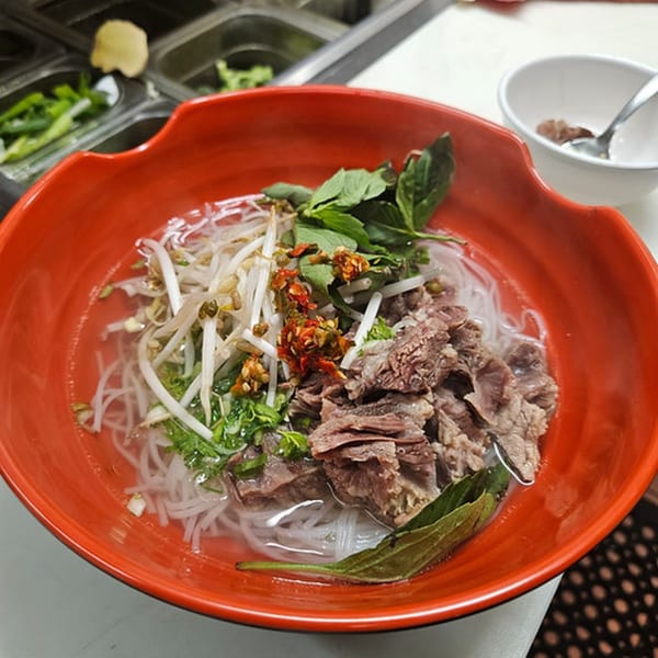 Laos beef noodle soup with sprouts, herbs, and chili in a red bowl at Sern Sapp Restaurant.